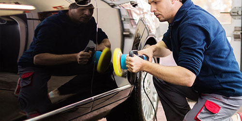 Two technicians machine-polishing a car