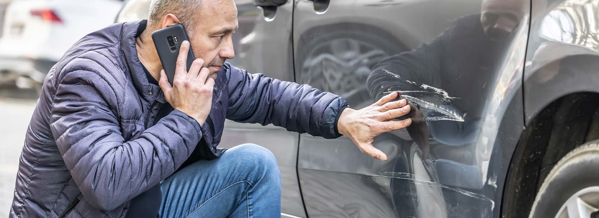 Driver on the phone inspecting a scratched car door after an accident