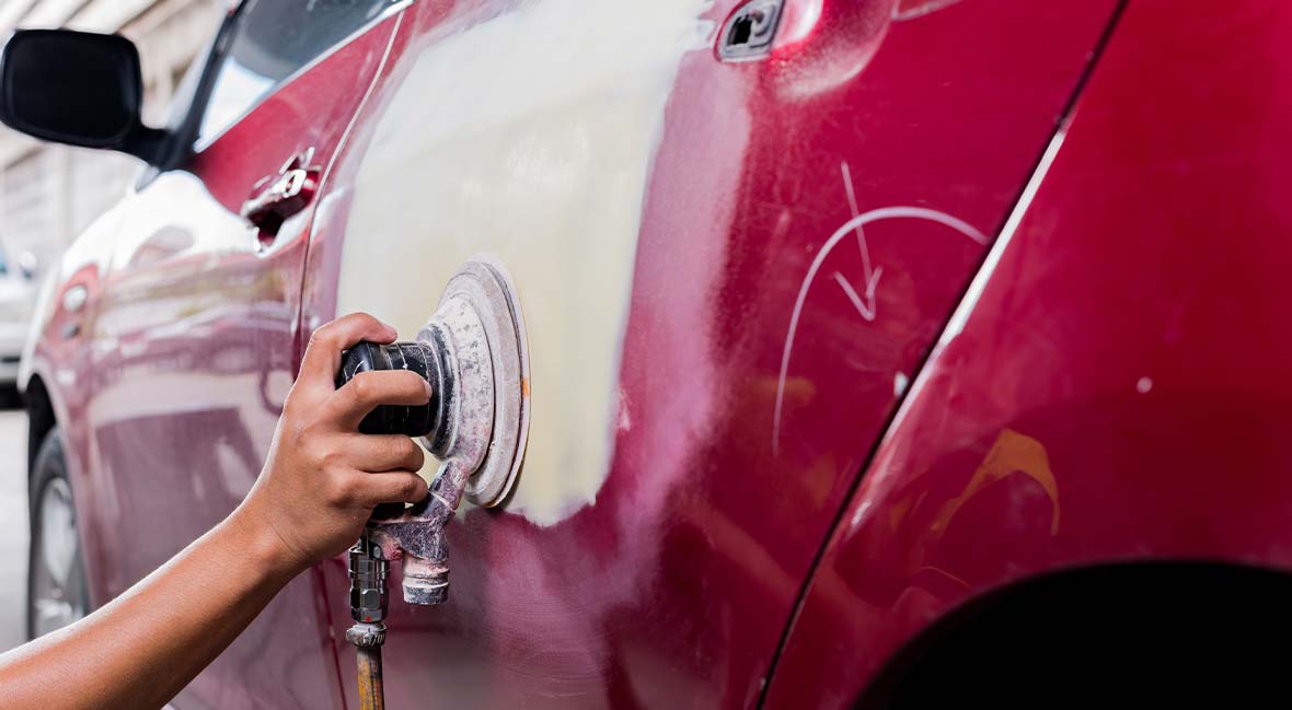 Technician repairing a dent on a red car panel